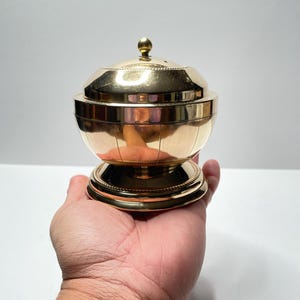 Peut inclure: Un br&ucirc;leur d'encens en m&eacute;tal dor&eacute; avec un couvercle rond et une base. Le br&ucirc;leur a un motif d&eacute;coratif sur le couvercle et la base.
