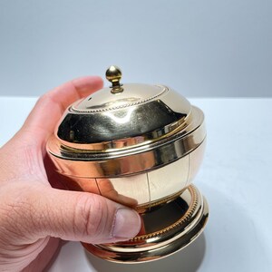 Peut inclure: Un r&eacute;cipient en m&eacute;tal dor&eacute; avec un couvercle bomb&eacute; et une base d&eacute;corative. Le r&eacute;cipient pr&eacute;sente un motif nervur&eacute; et une bordure perl&eacute;e autour du haut et du bas.