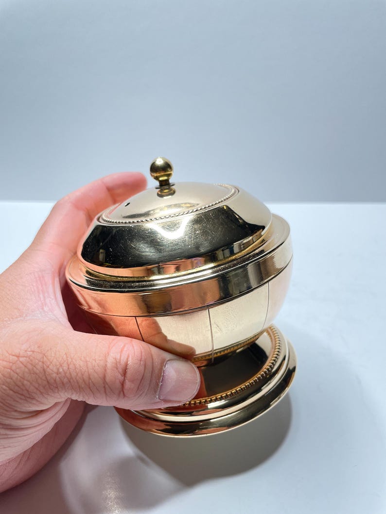Peut inclure: Un r&eacute;cipient en m&eacute;tal dor&eacute; avec un couvercle bomb&eacute; et une base d&eacute;corative. Le r&eacute;cipient pr&eacute;sente un motif nervur&eacute; et une bordure perl&eacute;e autour du haut et du bas.