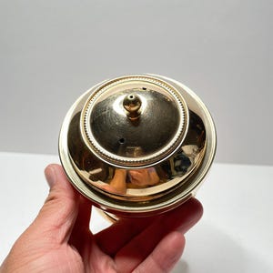 Peut inclure: Couvercle en m&eacute;tal dor&eacute; avec un petit bouton sur le dessus. Le couvercle a une bordure d&eacute;corative autour du bord.