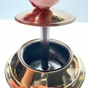 Peut inclure: Un cendrier en m&eacute;tal dor&eacute; avec un couvercle amovible. Le couvercle est orn&eacute; d'un motif de corde d&eacute;coratif autour du bord. Le cendrier a un cylindre central pour contenir les cigarettes.
