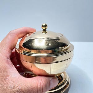 Peut inclure: Un r&eacute;cipient en m&eacute;tal dor&eacute; avec un couvercle bomb&eacute; et une base d&eacute;corative. Le r&eacute;cipient pr&eacute;sente un motif nervur&eacute; et un petit bouton sur le dessus du couvercle.
