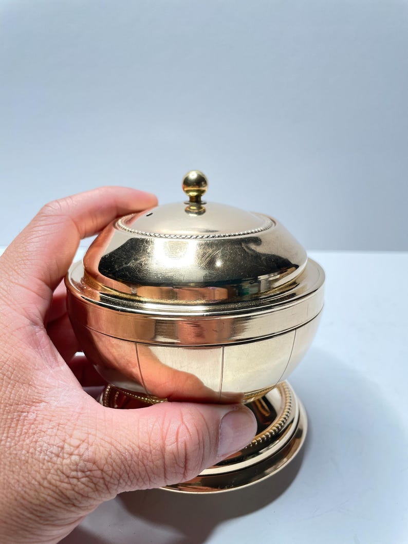Peut inclure: Un r&eacute;cipient en m&eacute;tal dor&eacute; avec un couvercle bomb&eacute; et une base d&eacute;corative. Le r&eacute;cipient pr&eacute;sente un motif nervur&eacute; et un petit bouton sur le dessus du couvercle.