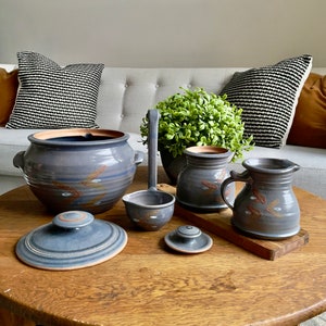 May include: A set of blue and brown pottery kitchenware, including a large pot with a lid, a small pitcher, a large pitcher, a ladle, and a small lid. The pottery is decorated with a simple design of white and brown lines.