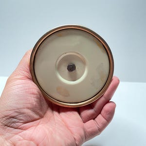 Peut inclure: Le dessous d'un bougeoir en c&eacute;ramique blanche avec une bordure dor&eacute;e. Le bougeoir a une petite vis en m&eacute;tal au centre.