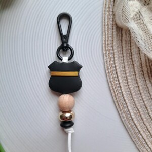 May include: Black and gold shield keyring with wooden and gold beads. The keyring has a black clip.