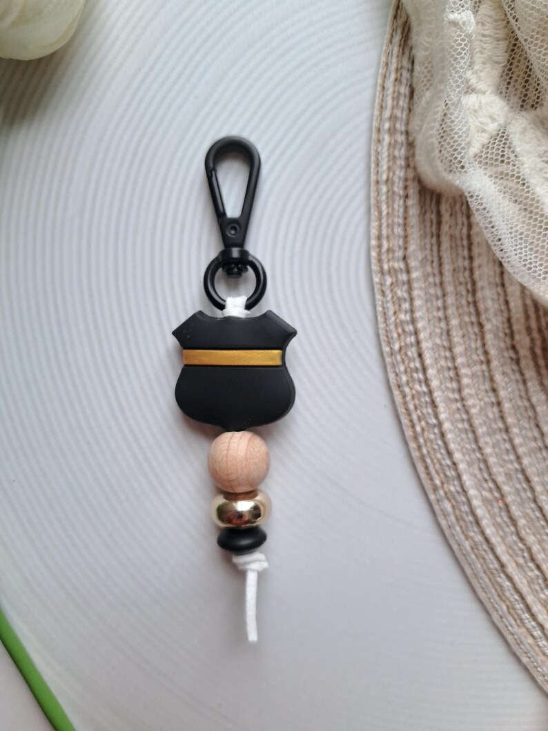 May include: Black and gold shield keyring with wooden and gold beads. The keyring has a black clip.
