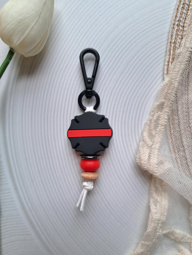 May include: Black and red silicone keychain with a thin red line across the centre. The keychain has a black metal clip and a wooden bead with a red silicone bead.