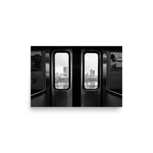 Black and white view of the Boston skyline framed by the doors of an MBTA train, looking out over the Charles River with the Prudential Tower and other city buildings in the distance.