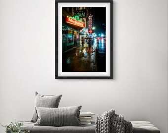 May include: A black and white photograph of a city street at night. The street is wet from rain and there are neon signs for a bar called "Michael's" and a restaurant called "TAM".