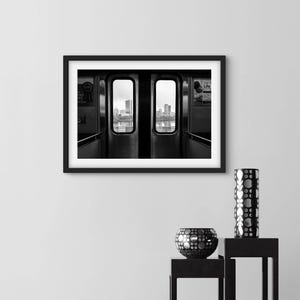 Può includere: Fotografia in bianco e nero di un finestrino di un vagone ferroviario con vista su uno skyline urbano. Il finestrino è incorniciato da una cornice nera e lo skyline urbano è visibile attraverso il finestrino.
