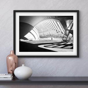 May include: Black and white photograph of a modern building interior with a large, arched ceiling and a grid of beams. The photo is framed in a black frame and is displayed on a wall.