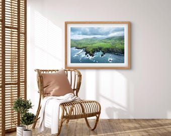 May include: An aerial photograph of a green, grassy coastline with a rocky shore and blue water. The sky is cloudy and the water is choppy.
