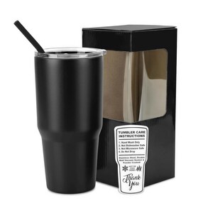 Op de afbeelding: Een matzwarte roestvrijstalen beker met een doorzichtig deksel en een zwart rietje, vergezeld van een zwarte geschenkdoos met een venster en een wit label met onderhoudsinstructies: Hand Wash Only, Not Dishwasher Safe, Not Microwave Safe, Do Not Drop.