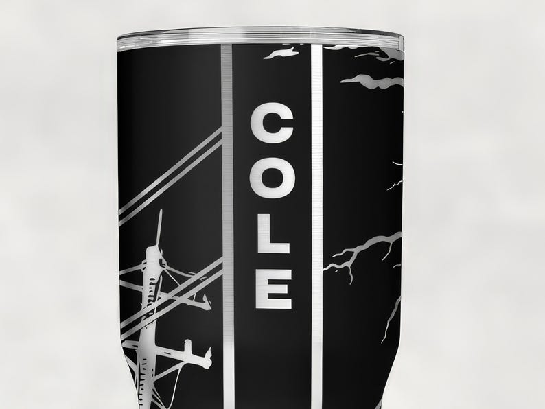 Op de afbeelding: Een zwarte cilindrische beker met een verticale witte streep met de naam COLE in dikke witte hoofdletters. Het ontwerp bevat een witte afbeelding van een elektriciteitsmast met lijnen aan de linkerkant en een silhouet van een tak aan de rechterkant.