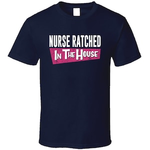May include: Navy blue t-shirt with white text that reads "Nurse Ratched In The House" in a pink rectangle.