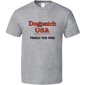 May include: A heather gray t-shirt with the words "Dogpatch USA" in red and black lettering. Below the text, it reads "Dogpatch, Arkansas" and "Family Fun Park". The shirt has a crew neck and short sleeves.