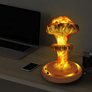 Könnte beinhalten: Eine pilzförmige Lampe mit einem leuchtenden orange-gelben Licht, das an eine Nuklearexplosion erinnert. Die Lampe steht auf einem Holzsockel mit einem runden Design.