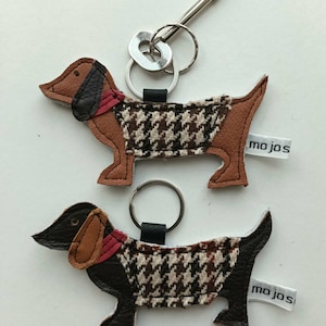 May include: Two brown and black dachshund dog keychains with red collars and a houndstooth pattern. Each keychain has a silver key ring and a white tag with the text "mojos".