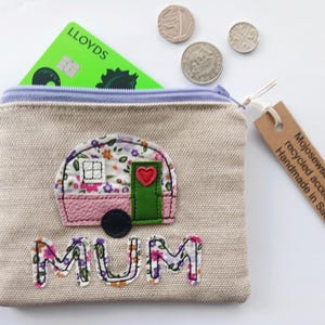 May include: A beige canvas purse with a floral caravan design and the word "MUM". The purse has a light blue zip and a green credit card inside. Several coins are visible. Handmade in Saddleworth.