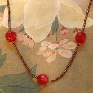 May include: A necklace with a brown chain and three red glass beads. The necklace is on a floral patterned background.