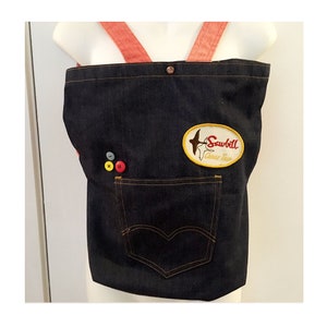 May include: A blue denim tote bag with red straps and a patch that says "Sawbill Canoe Trip". The bag has a pocket on the front and a few buttons.