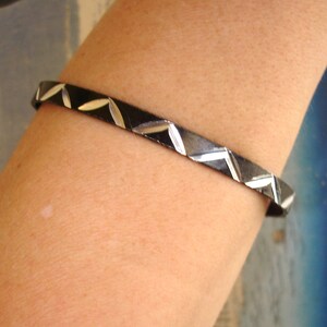 May include: A black and silver bangle bracelet with a geometric pattern. The bracelet is made of metal and has a polished finish.