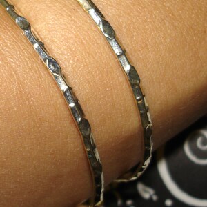 May include: Two silver bangles with a textured design. The bangles are stacked on a person's wrist.