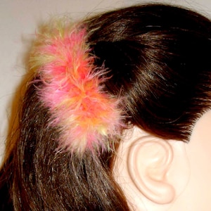 May include: A pink and yellow feather hair clip. The clip is in a woman's hair.