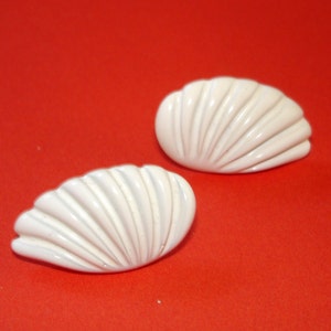 May include: A pair of white shell-shaped earrings. The earrings are made of a smooth, white material and have a slightly curved shape.