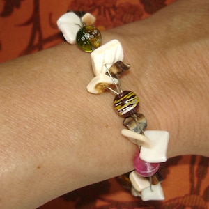May include: A white and brown beaded bracelet with colorful glass beads. The bracelet is made with wire and has a variety of shapes and sizes of beads.