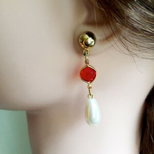 May include: Gold dangle earrings with a red faceted gemstone and a white pearl drop.