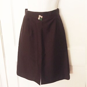 May include: A brown skirt with a small embroidered flower design on the front.