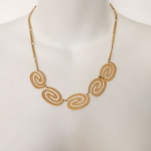 May include: A gold chain necklace with five oval-shaped pendants. Each pendant is a cutout design of a spiral.