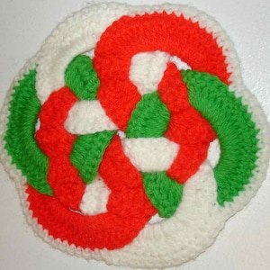 May include: A crocheted trivet with a white, red, and green design. The trivet is made of yarn and has a circular shape.