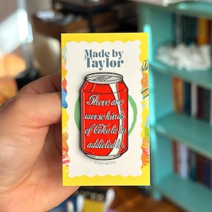 以下が含まれることがあります： 白いストライプと「There are worse kinds of Coke to be addicted to.」という文字が入った、赤いソーダ缶の形をしたエナメルピン。ピンは「Made by Taylor」と「Enamel Pin」と印刷された黄色い台紙に取り付けられています。