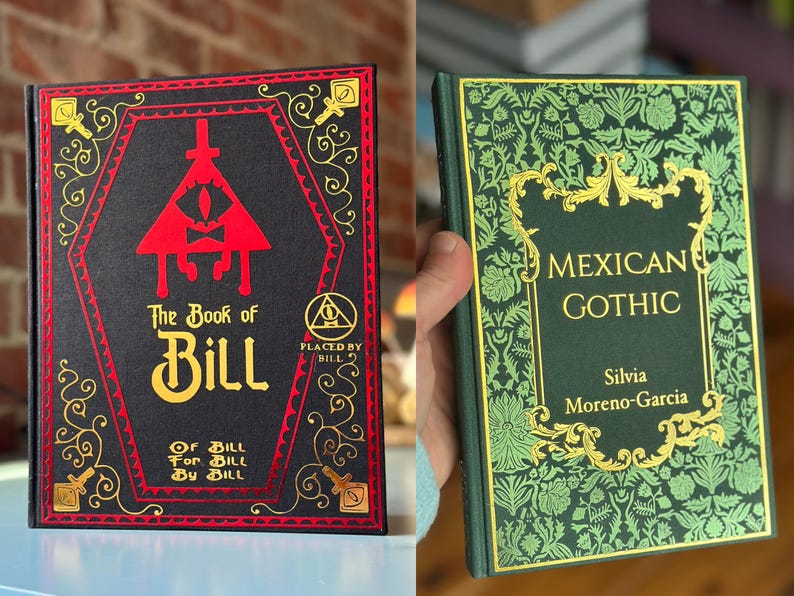 Op de afbeelding: Twee hardcover boeken. De eerste, "The Book of Bill", heeft een zwarte kaft met rode en gouden accenten, met een rood driehoekig oogontwerp. Het tweede boek, "Mexican Gothic", heeft een groene kaft met gouden bloempatronen en tekst.