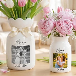 Puede incluir: Dos jarrones de cerámica blanca con arreglos florales. Uno contiene tulipanes rosas y blancos, el otro peonías rosas. Cada jarrón tiene una foto, las palabras "Mama I Love You" y un nombre. Una cinta beige adorna un jarrón.