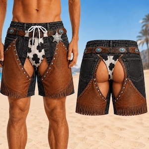 May include: Chaps-style shorts featuring a black denim waistband with a brown belt, turquoise accents, and a silver star badge labelled Outlaw. The design includes brown leather-look panels with fringe, silver studs, and a white cow-print fabric insert.