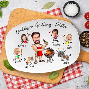 May include: A white oval ceramic plate featuring the text Daddy's Grilling Plate and a cartoon illustration of a person in a red apron grilling, surrounded by smaller cartoon figures labeled Kitty, Bobby, Lizzie, Dash, Garfield, and Sadie.