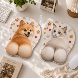 May include: Two ergonomic mouse pads featuring animal designs. The left pad displays a tan Pomeranian dog with a raised bottom section, while the right pad shows a white and grey cat with a raised bottom section. Both pads have paw prints, bones, and red hearts.