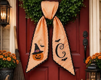 May include: A decorative orange and white striped fabric door hanger featuring a black scalloped edge. One side displays a jack-o'-lantern wearing a witch hat with a crescent moon and bat, while the other side features a large letter C with bats.