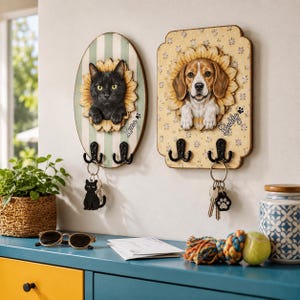 Puede incluir: Dos soportes de pared de madera para llaves con retratos de mascotas. El tablero ovalado muestra un gato negro con el nombre Luna, mientras que el rectangular muestra un beagle con el nombre Buddy. Ambos tienen marcos de girasol y dos ganchos.