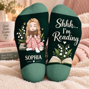May include: A pair of dark green socks featuring a graphic of a person with blonde hair reading a book, lily of the valley flowers, and the name Sophia on one sock, and the text Shhh... I'm Reading with an open book and flowers on the other.