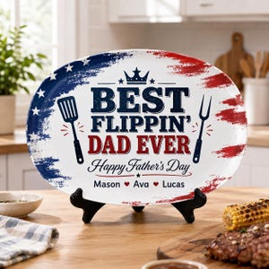 May include: Oval serving platter with a patriotic design. The white platter features a blue and red border with the text "BEST FLIPPIN' DAD EVER" and "Happy Father's Day". Includes names and heart symbols. A spatula and fork are also featured.