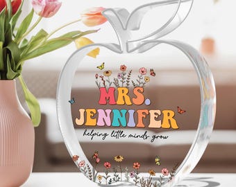 May include: A clear glass apple shaped paperweight with a colorful floral design and the text "MRS. JENNIFER helping little minds grow".