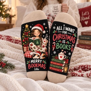 Op de afbeelding: Een paar zwarte sokken met beige hielen en tenen. Eén sok toont een meisje met een kerstmuts dat leest met een kat, een kerstboom en de tekst Merry Bookmas Lila. De andere toont de tekst All I want for Christmas is books met een stapel boeken, een mok en zuurstokken.