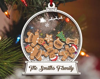 Puede incluir: Adorno navideño personalizado con un diseño de bola de nieve, con figuras de pan de jengibre y otras formas festivas. El adorno incluye el texto "The Smiths Family" y el año "2025".