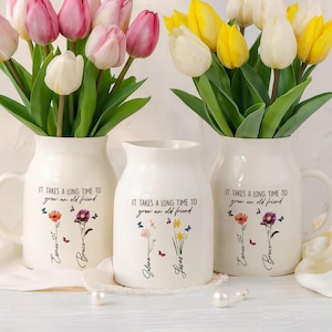 May include: Three white ceramic vases with a floral design and the text "It takes a long time to grow an old friend". Each vase has a different floral design and two names written below the flowers. The names are Esmee and Bruce, Selena and Jusas, and Esmee and Bruce.