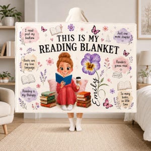 May include: A cream-colored fleece blanket featuring the text 'THIS IS MY READING BLANKET' and 'Emily'. It displays a cartoon character reading a book, stacks of books, butterflies, flowers, and phrases like 'I read past my bedtime'.